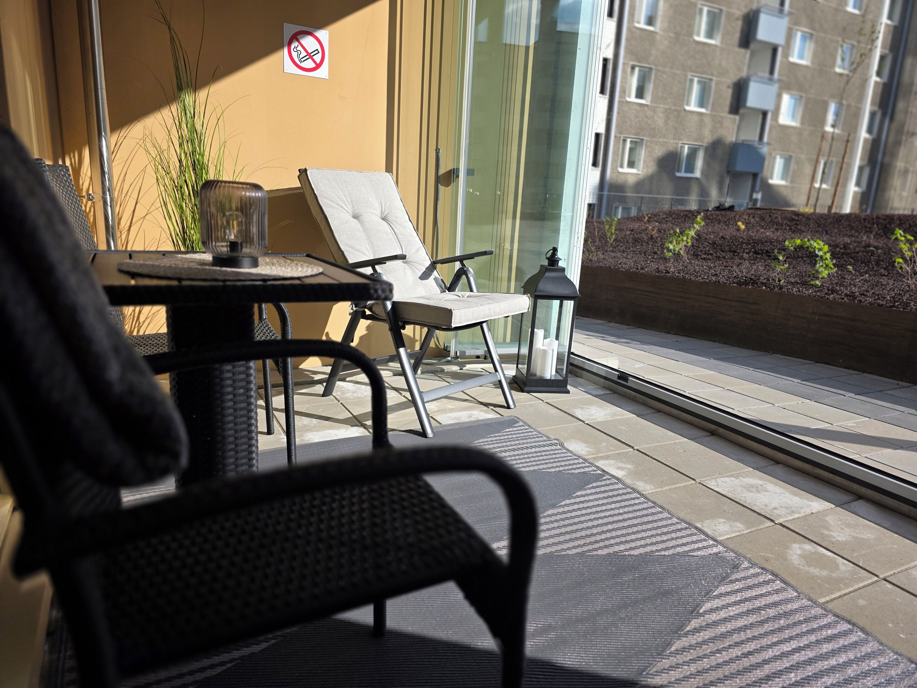 A balcony with a table, two chairs, a potted plant, and a lantern.