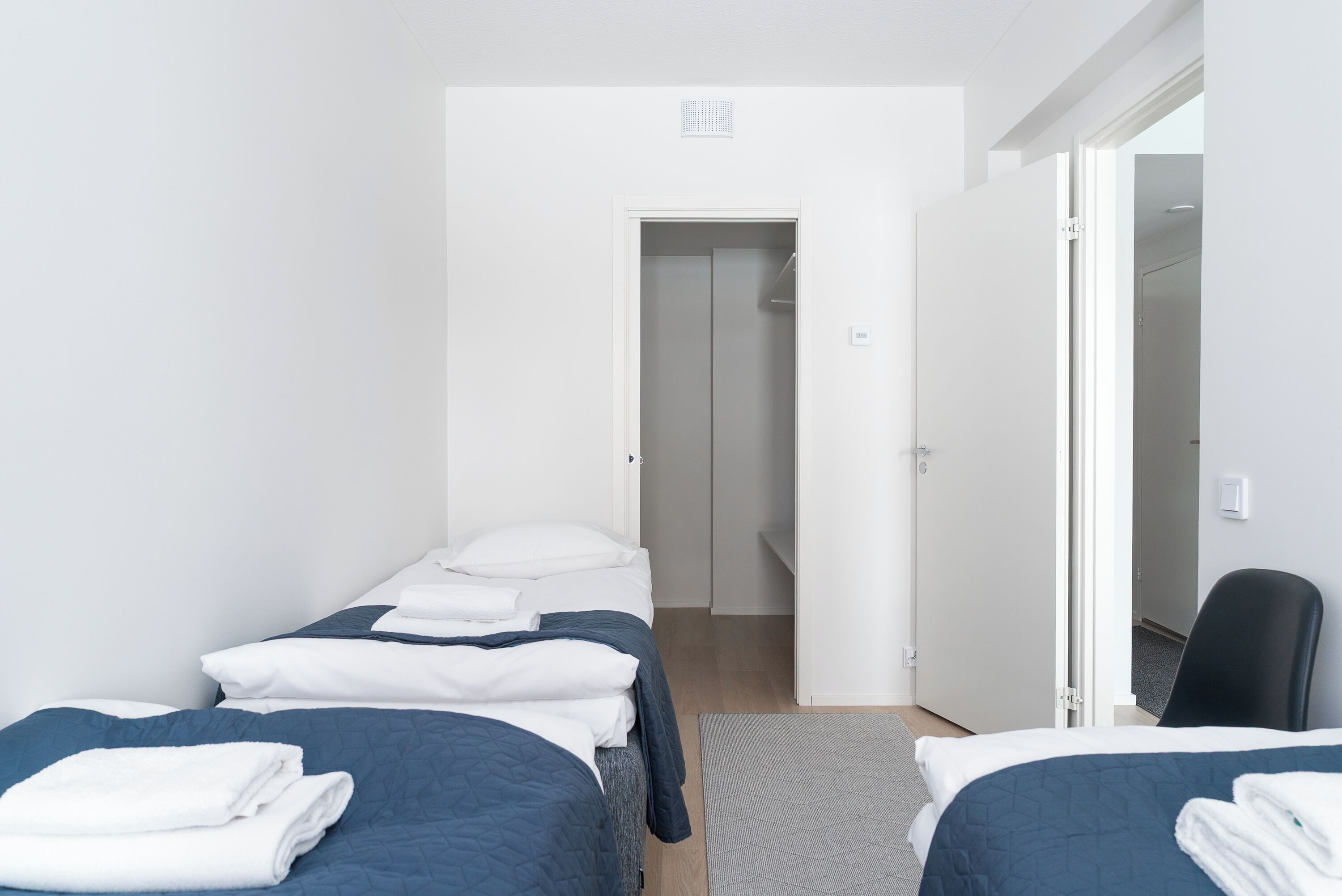 A hotel room with two beds, a chair, and a door leading to another room.