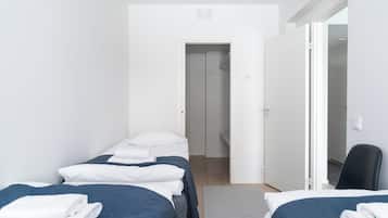 A hotel room with two beds, a chair, and a door leading to another room.
