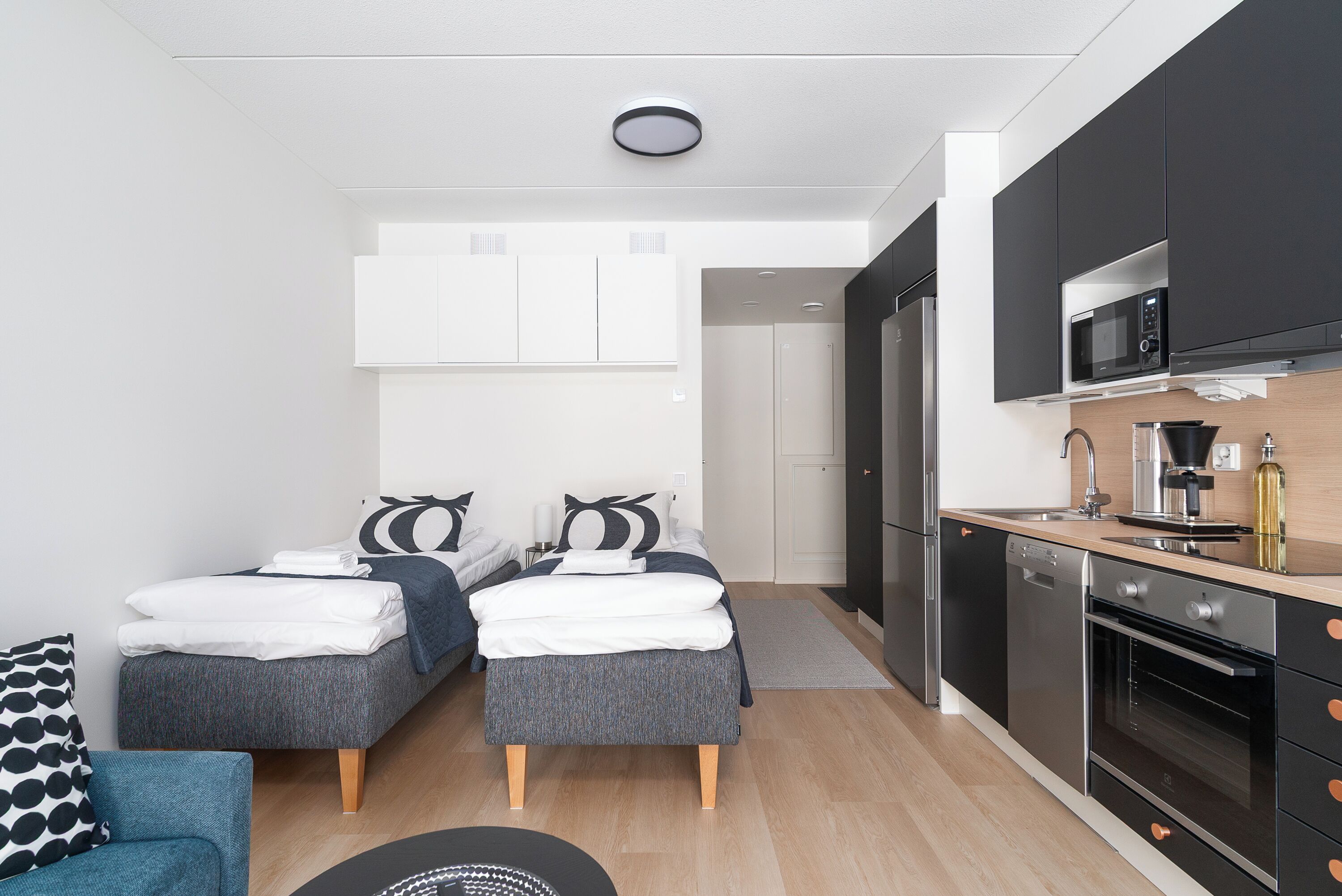 A modern apartment with two beds, a kitchenette, and a bathroom.