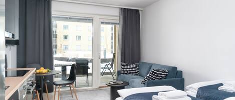 A modern hotel room with a kitchenette, a sofa bed, a dining area, and a view of the city.