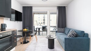 Eine moderne Wohnung mit Küche, Essbereich und Wohnzimmer. Sie verfügt über einen Flachbildfernseher, einen Esstisch mit Stühlen, ein Sofa mit gemusterten Kissen und einen kleinen runden Tisch mit einem dekorativen Gegenstand.