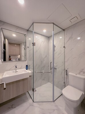 A modern bathroom with a glass-enclosed shower, a white sink, and a toilet.