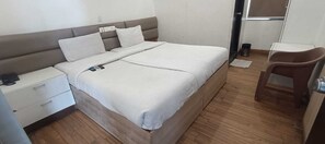 Habitación individual con piso de madera, una mesita de noche con lámpara, una silla y una pequeña mesa.
