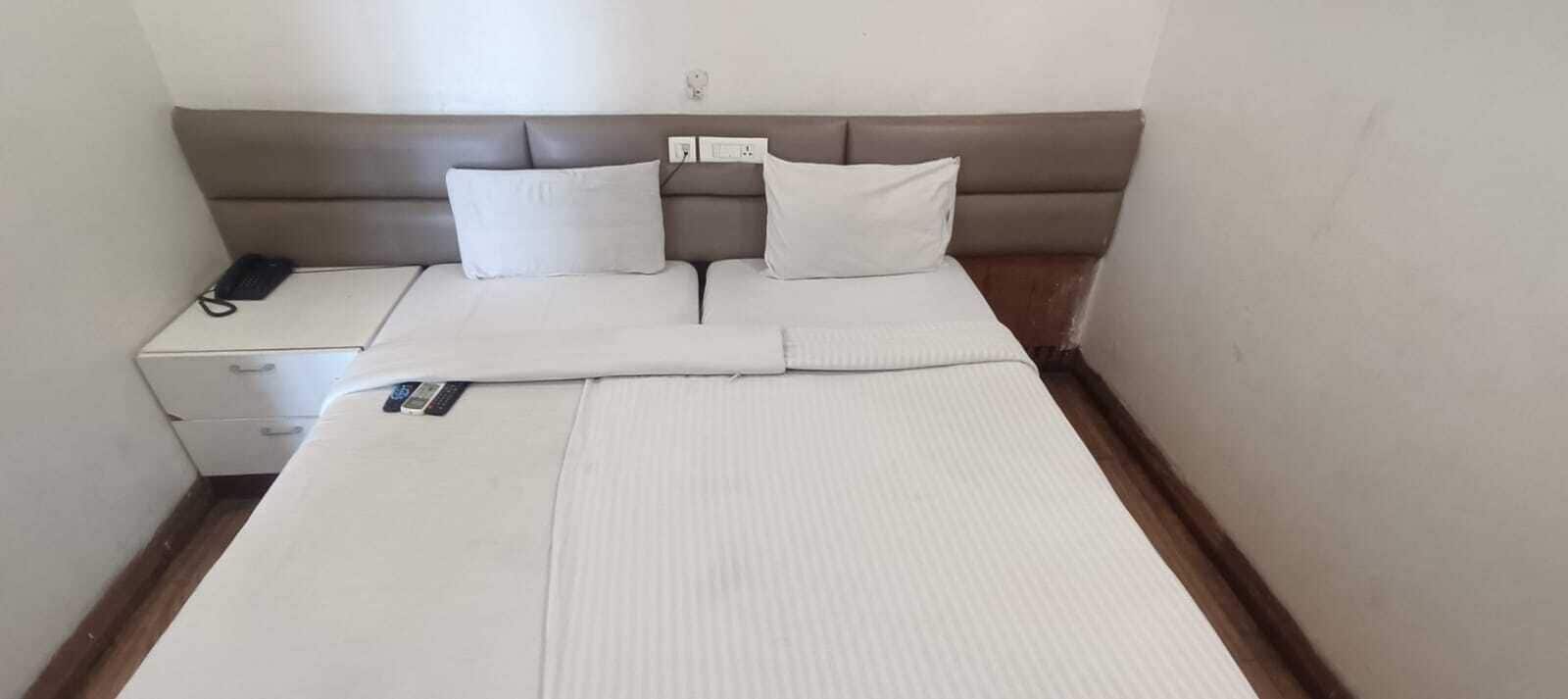 A neatly made bed with white linens, a bedside table with a phone, and a wall socket.