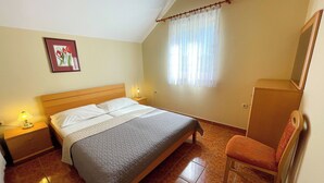 Une chambre à coucher avec un lit, des tables de chevet, une chaise, un tableau et une fenêtre avec des rideaux.