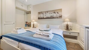 A hotel room with a bed, two bedside tables with lamps, a bookshelf, and a painting on the wall. - Spacious 3-room apartment on approx. 80 m² for up to 4 people in Westerland (Westerland)