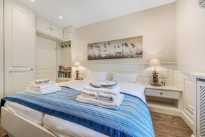 A hotel room with a bed, two bedside tables with lamps, a bookshelf, and a painting on the wall. - Spacious 3-room apartment on approx. 80 m² for up to 4 people in Westerland (Westerland)