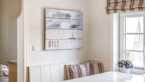 Comedor con una mesa blanca, cojines a rayas y un cuadro en la pared que muestra un velero.