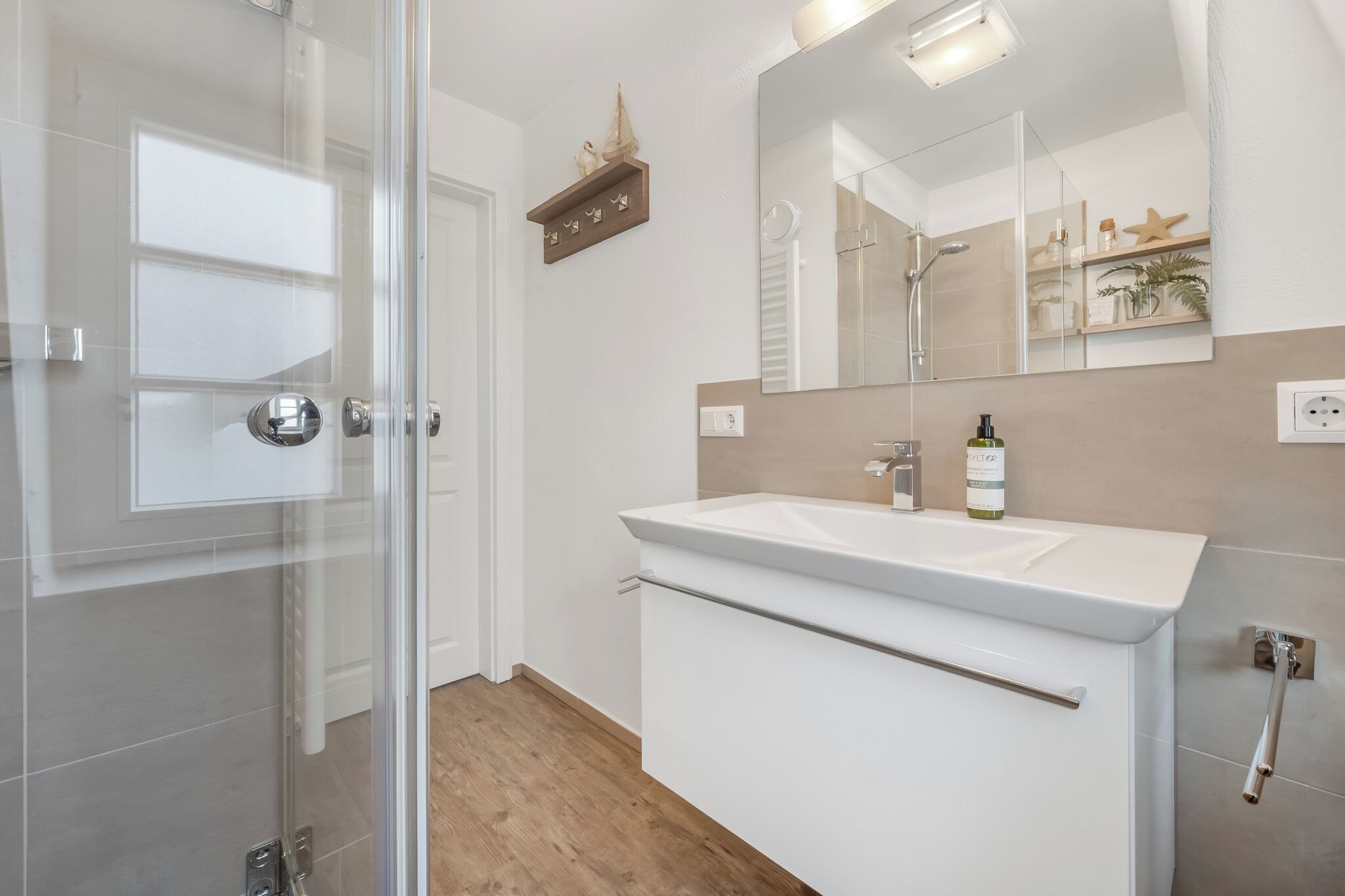 Een moderne badkamer met een glazen douchedeur, een witte wastafel en een grote spiegel.