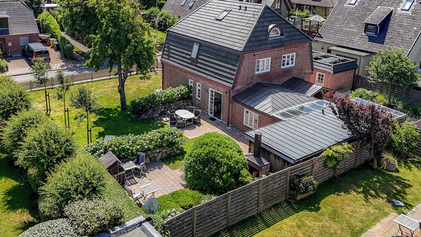 Una casa residencial con techo inclinado, patio trasero cercado y zona de patio.