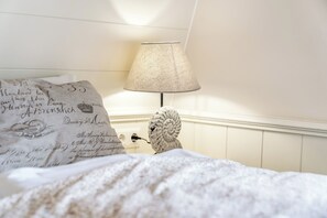 Een opgemaakt bed met een decoratief kussen en een lamp met een gestructureerde lampenkap.