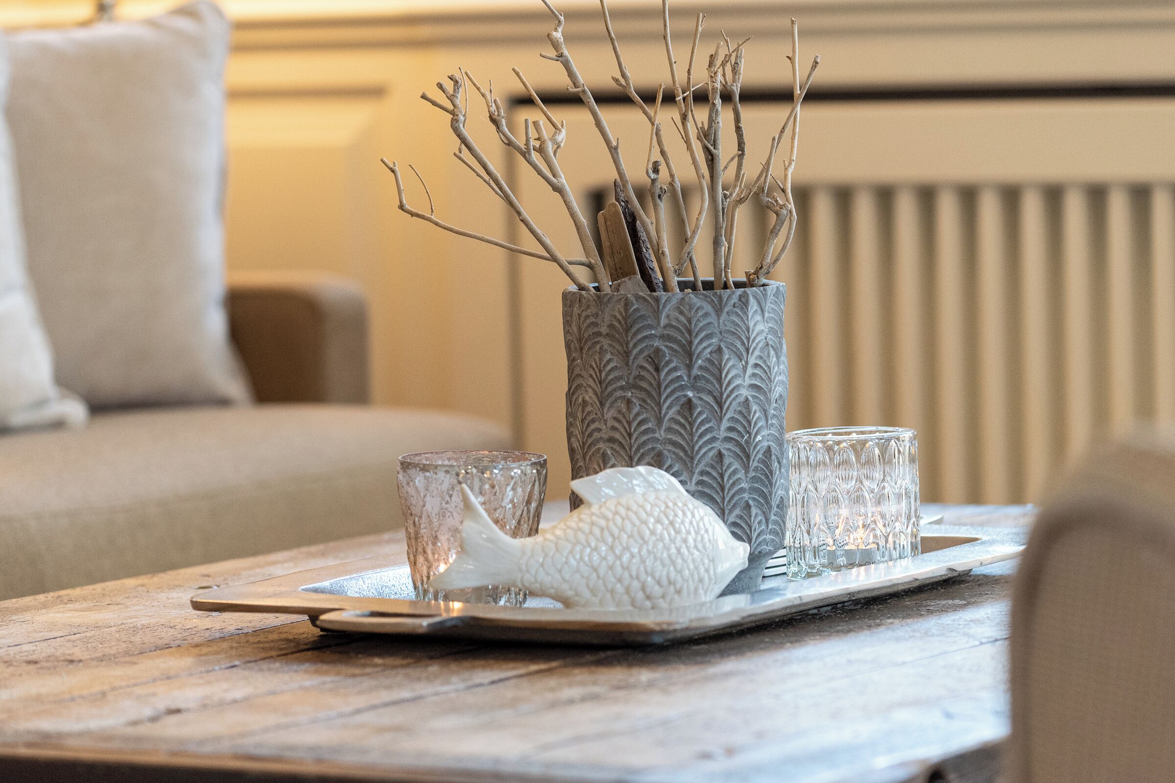 A tray with a fish-shaped salt shaker, two clear glasses, and a vase with branches on a wooden table.