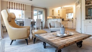 A living room with a sofa, armchair, and coffee table, a dining area with a table and chairs, and a kitchen with cabinets and a television. - Bright 3-room apartment with approx. 70 m² for up to 4 people (Westerland)