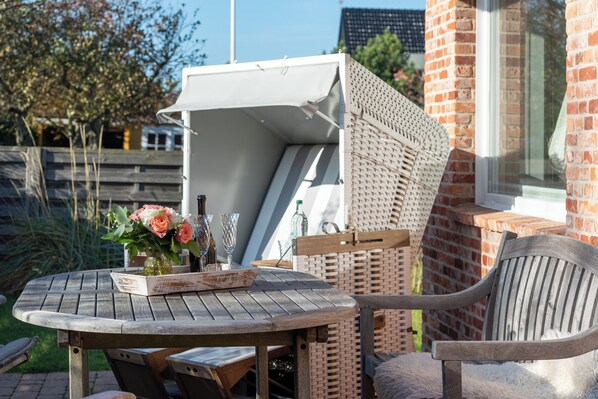 A round wooden table with a white umbrella, a wicker chair, and a vase with flowers. - Beautiful 2-room vacation apartment on the first floor with approx. 40 m² for up to 2 people (Westerland)