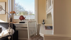 A room with a window, a radiator, a chair, a desk, and a lamp. - Beautiful 2-room vacation apartment on the first floor with approx. 40 m² for up to 2 people (Westerland)