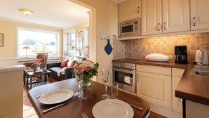 A modern kitchen with white cabinets, a microwave, and a coffee maker. There is a dining table with plates and glasses. - Beautiful 2-room vacation apartment on the first floor with approx. 40 m² for up to 2 people (Westerland)