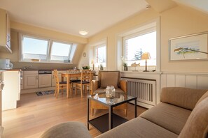 A cozy living room with a glass coffee table, a sofa, and a dining area with a table and chairs. - Beautiful 2-room vacation apartment on the top floor, approximately 40 m², for 2 people (Westerland)