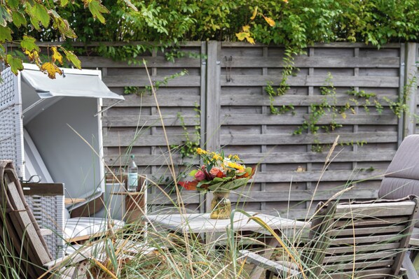 Een tuin met een houten omheining, een tafel met een bloevas en tuinmeubilair.