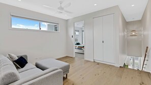 En moderne stue med en grå sofa, en loftventilator, et stort vindue og udsigt til et andet rum.