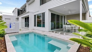 Et moderne hus i to etager med swimmingpool, store vinduer og en patio.