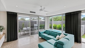 A modern living room with a teal sofa, a ceiling fan, and large sliding glass doors leading to an outdoor patio.