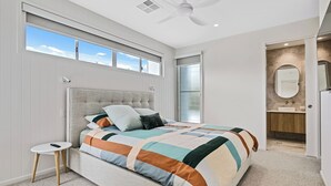 Ein Schlafzimmer mit Bett, einem kleinen Tisch, einem Deckenventilator und einem Badezimmer mit Spiegel und Waschbecken.