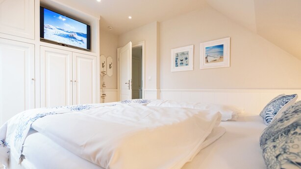 A bedroom with a bed, a TV mounted above it, and two framed pictures on the wall. - Bright 3-room holiday apartment on approx. 100 m² for up to 4 people (Westerland)