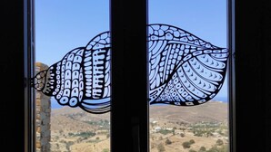 A window with a decorative black and white pattern, overlooking a hilly landscape with sparse vegetation. - Kea's Hidden Diamond (Otzias)