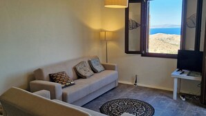 A living room with a sofa, armchair, and a television on a stand. - Kea's Hidden Diamond (Otzias)