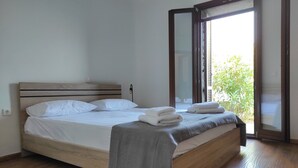 A bedroom with a wooden bed, white bedding, and a grey blanket. - Kea's Hidden Diamond (Otzias)
