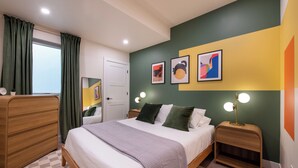 A bedroom with a bed, wooden dresser, bedside tables, and artwork on the wall. - Trendy Tennyson Flat (Denver)