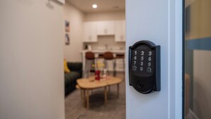 A modern entry door with a keypad lock, leading into a room with a dining area and kitchen in the background. - Trendy Tennyson Flat (Denver)