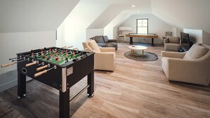 Una acogedora sala de estar tipo loft con mesa de fútbol, asientos cómodos y mesa de billar.