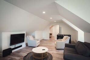 Ein modernes Wohnzimmer mit Fernseher, zwei weißen Sesseln, einem dunklen Sofa und einem runden Couchtisch.