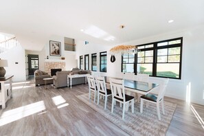 A spacious living area with a fireplace, a dining table with chairs, and large windows providing natural light.
