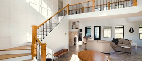 A spacious living area with a wooden staircase, a stone fireplace, and a large sofa.