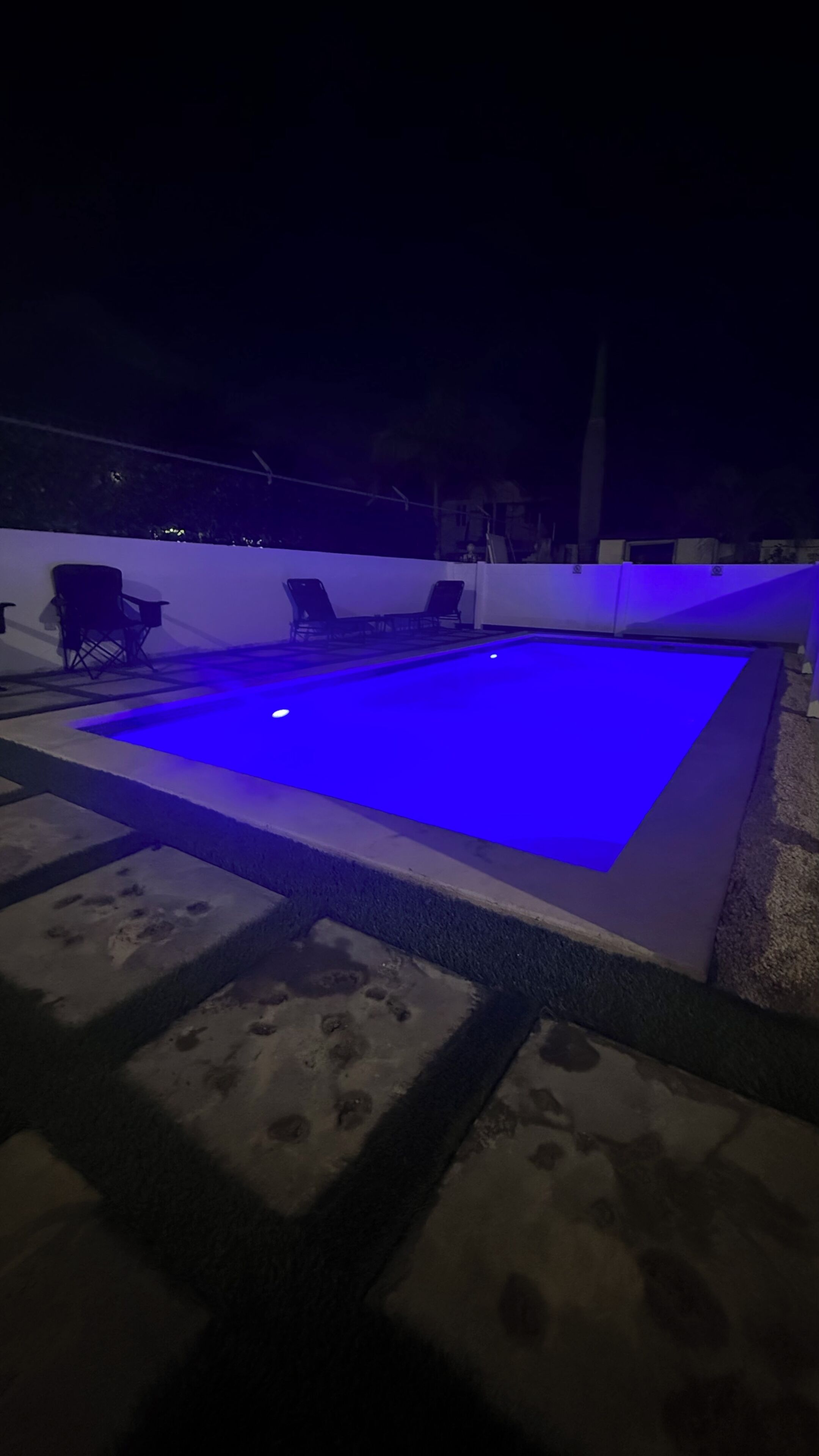A swimming pool with a blue light, surrounded by steps and chairs.