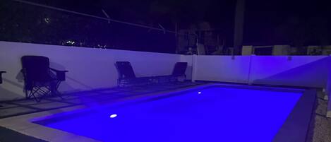 A swimming pool with a blue light, surrounded by steps and chairs.