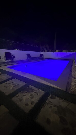 Une piscine éclairée de lumière bleue, entourée de marches et de chaises.