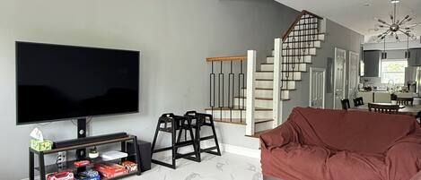 Ein modernes Wohnzimmer mit Flachbildfernseher, Deckenventilator, Treppe und Küchenzeile.