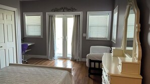 Un dormitorio con cama, cómoda, silla, escritorio y dos ventanas con persianas.