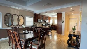 Un comedor amplio con una gran mesa de madera y sillas, una cocina al fondo y un espejo decorativo en la pared.