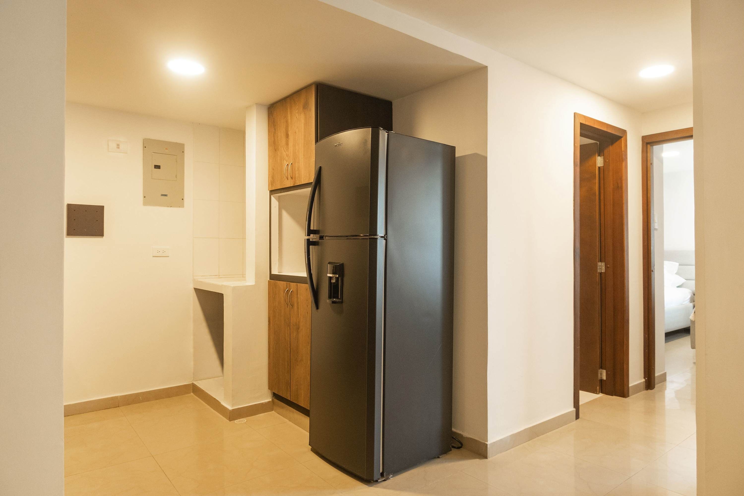 A kitchen with a black refrigerator, wooden cabinets, and a tiled floor.