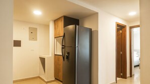 A kitchen with a black refrigerator, wooden cabinets, and a tiled floor. - w* | Delightful 2BR in Bocagrande (Cartagena de Indias)