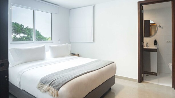 A bedroom with a large bed, a bedside table, a mirror, and a window. - w* | Delightful 2BR in Bocagrande (Cartagena de Indias)