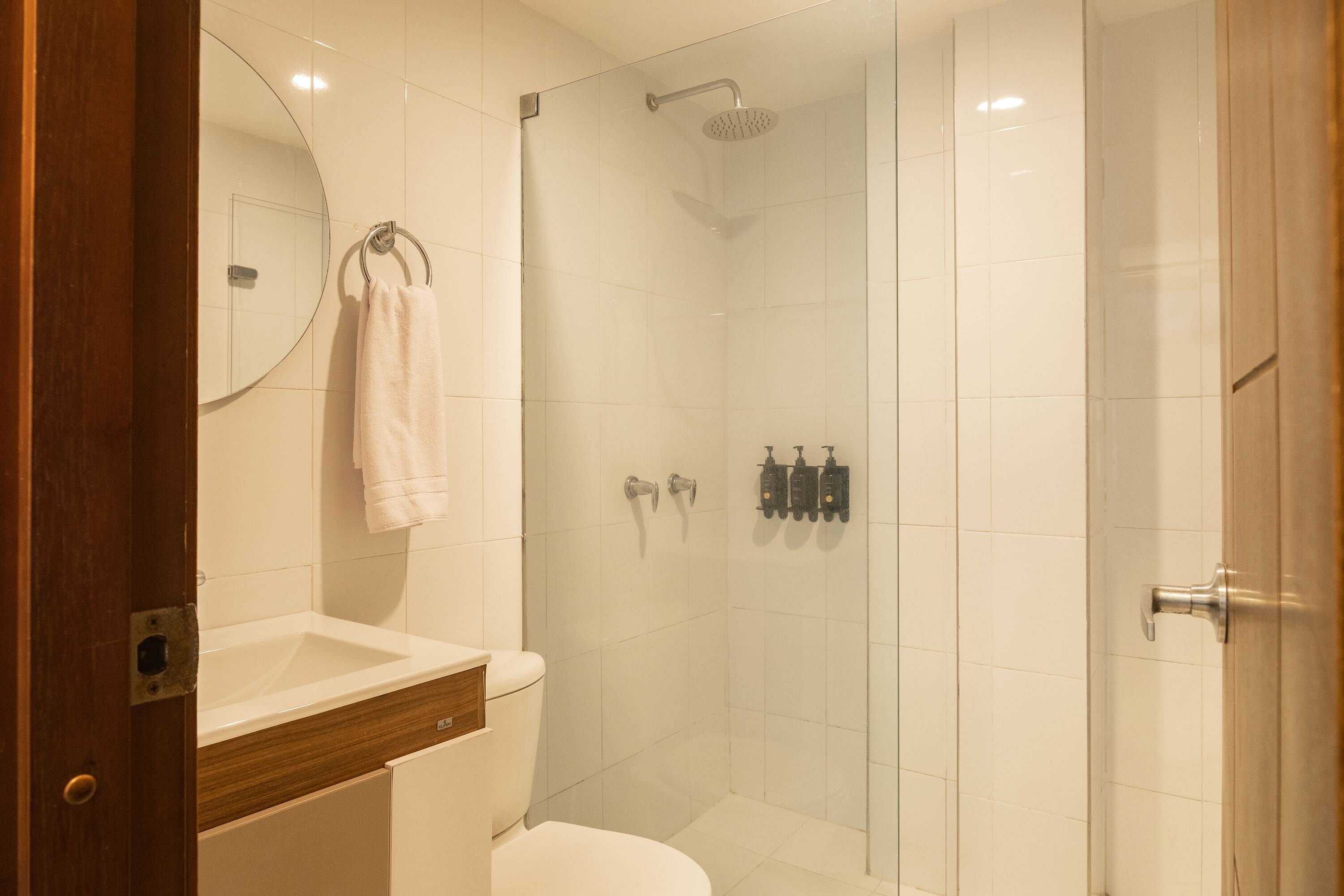 Un baño moderno con ducha de vidrio, lavamanos blanco y retrete.