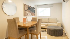 A modern living room with a wooden dining table, four chairs, a grey ottoman, a sofa, a round mirror, and a painting on the wall. - w* | Delightful 2BR in Bocagrande (Cartagena de Indias)