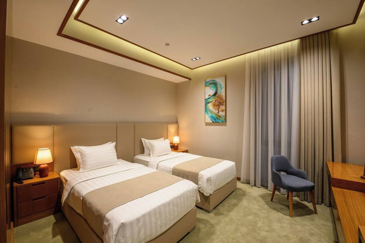 A hotel room with two beds, a desk, a chair, and a painting on the wall.