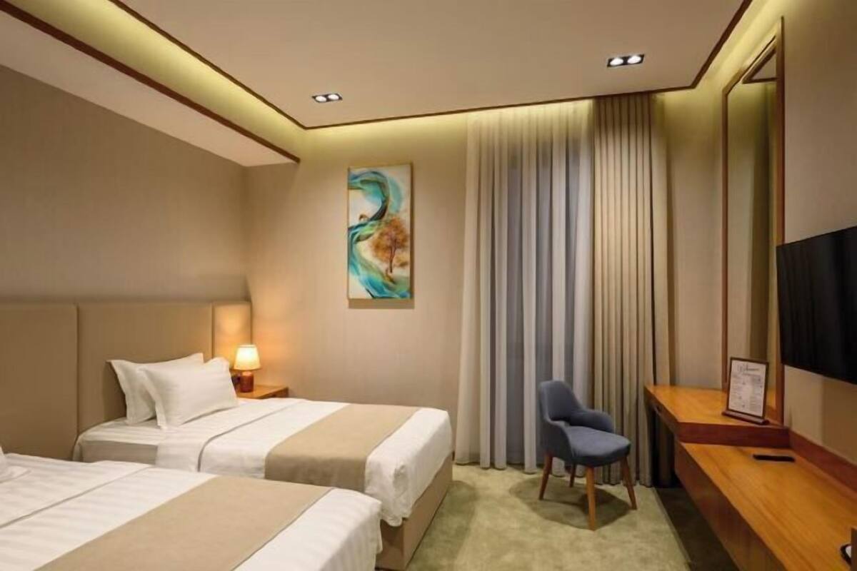 A hotel room with two beds, a desk, a chair, a TV, and a painting on the wall.